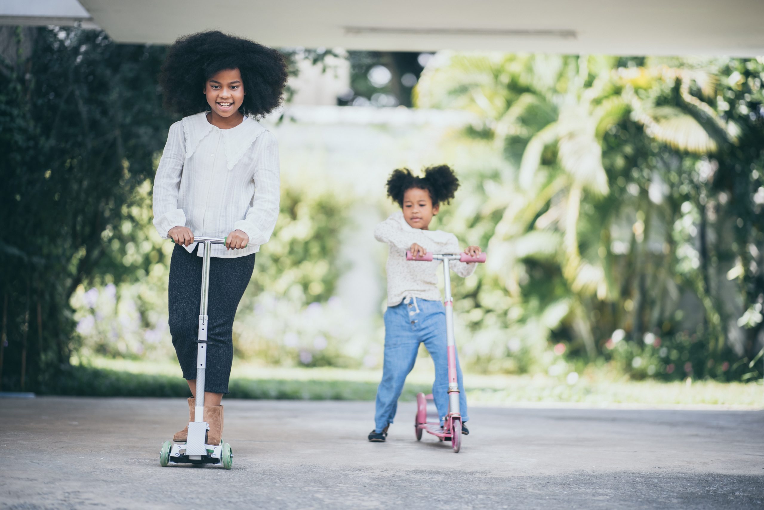children riding a scooters on the street, kid playing together, afro African American children riding a scooters during sunny on the street, kid playing together, afro afican american sibling, brother and sister outdoor activity concept, family time.