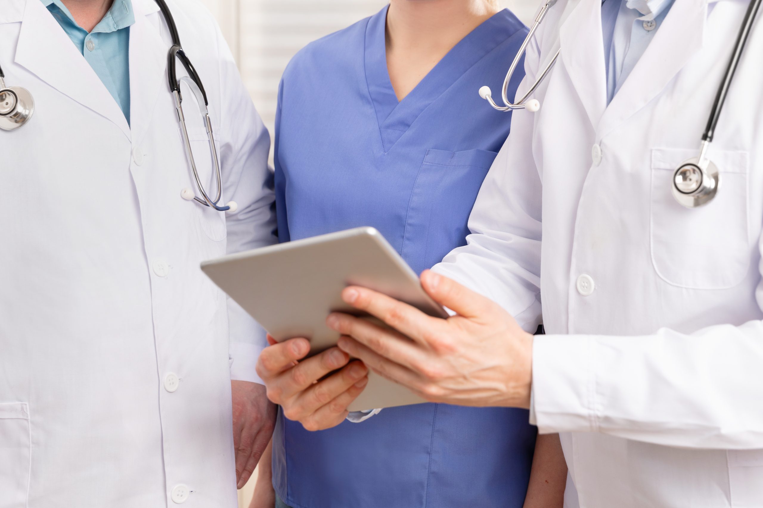 Doctor and medical team discussing patient report at tablet computer in hospital Doctor standing and discussing reports or x-ray image with medical team of nurse and doctors about a patient at tablet computer in hospital. Technology in healthcare services.